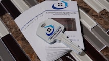 A stack of brochures for Cottonwood Apartments is placed on a tiled surface. On top of the brochures, there is a key with a logo that features a house and the words 'Apartments Near Me'. The brochures include contact information and a picture of the apartment interior.