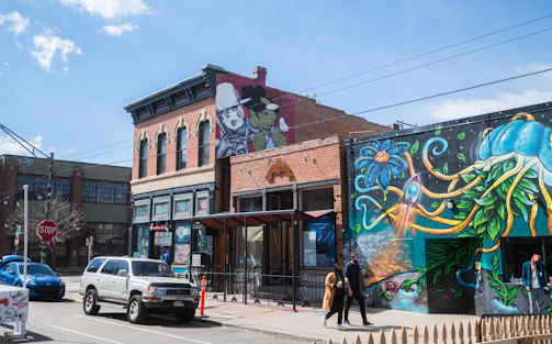 A bustling Philadelphia neighborhood scene with people walking and colorful murals on brick walls.
