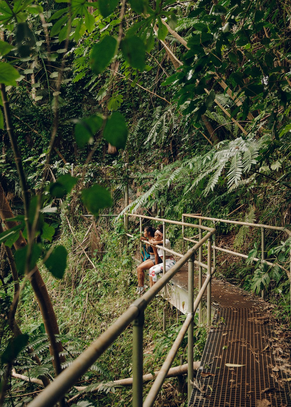 woman in white t-shirt and black shorts sitting on brown wooden bridge during daytime