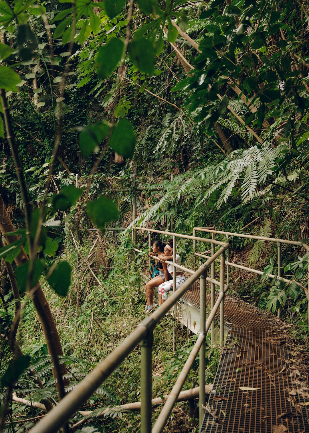 woman in white t-shirt and black shorts sitting on brown wooden bridge during daytime