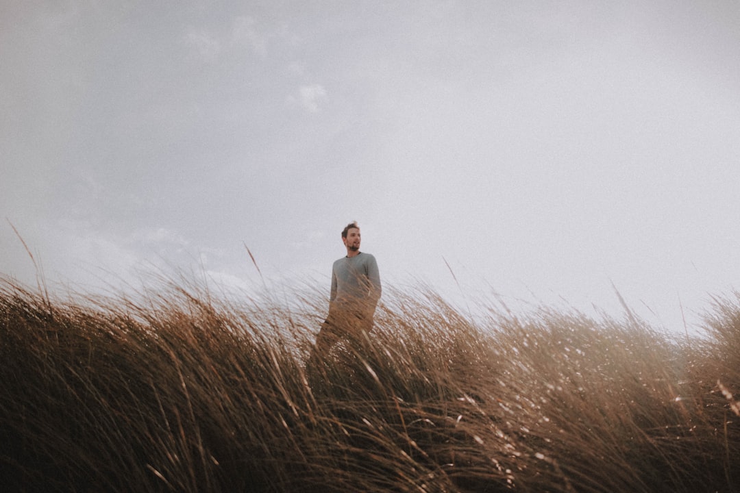 man in white thobe standing on brown grass field under white cloudy sky during daytime