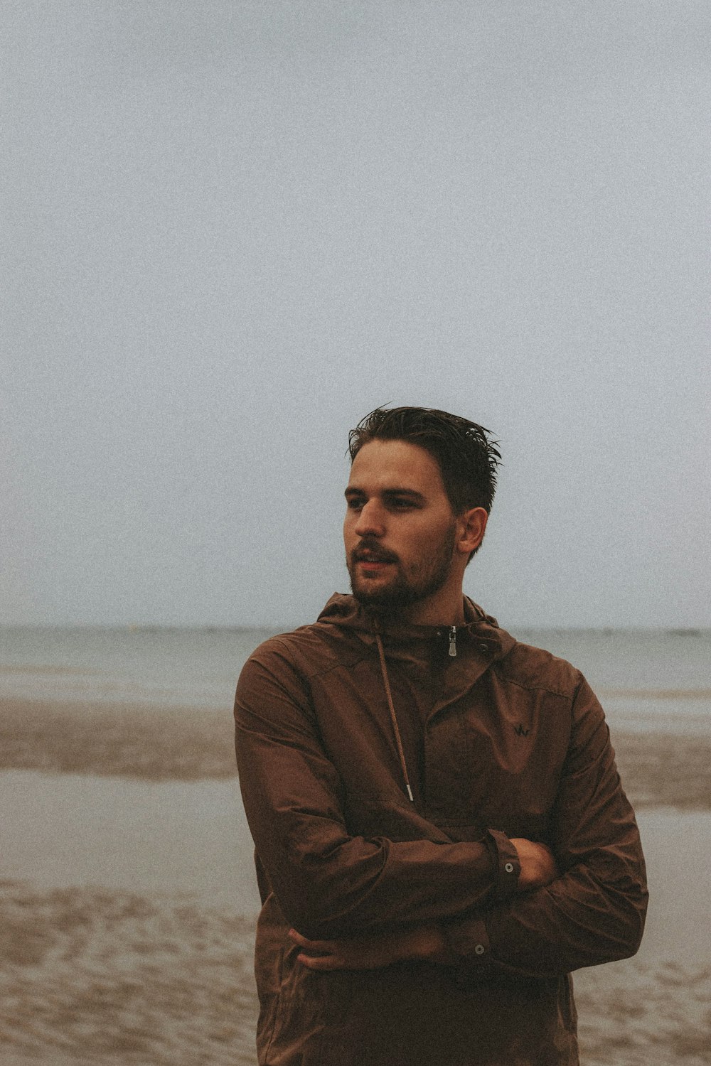 man in brown zip up jacket standing on beach during daytime