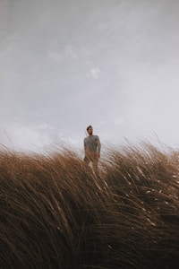 man in white dress shirt standing on brown grass field under white cloudy sky during daytime