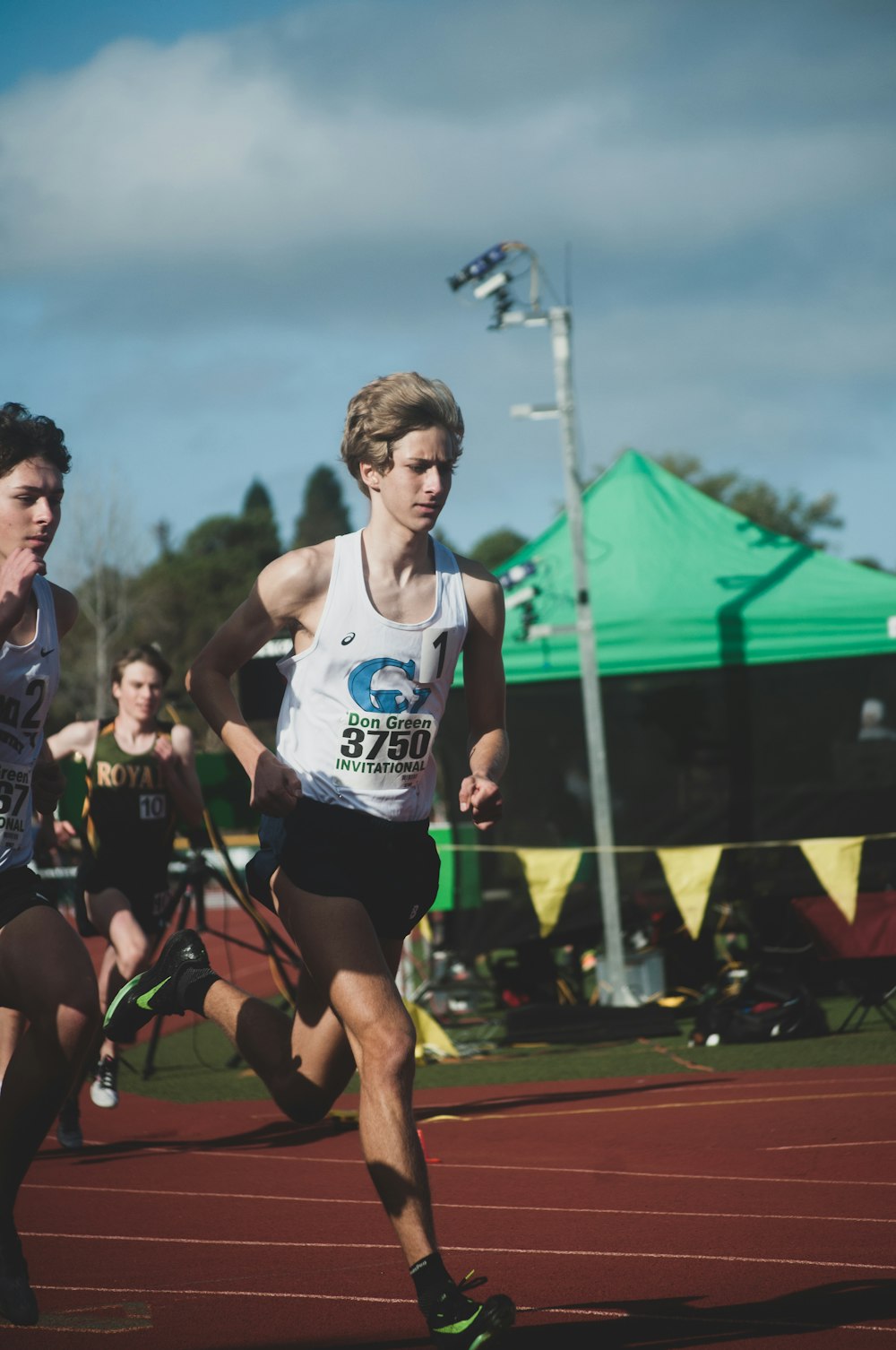 man in white tank top running on track field during daytime