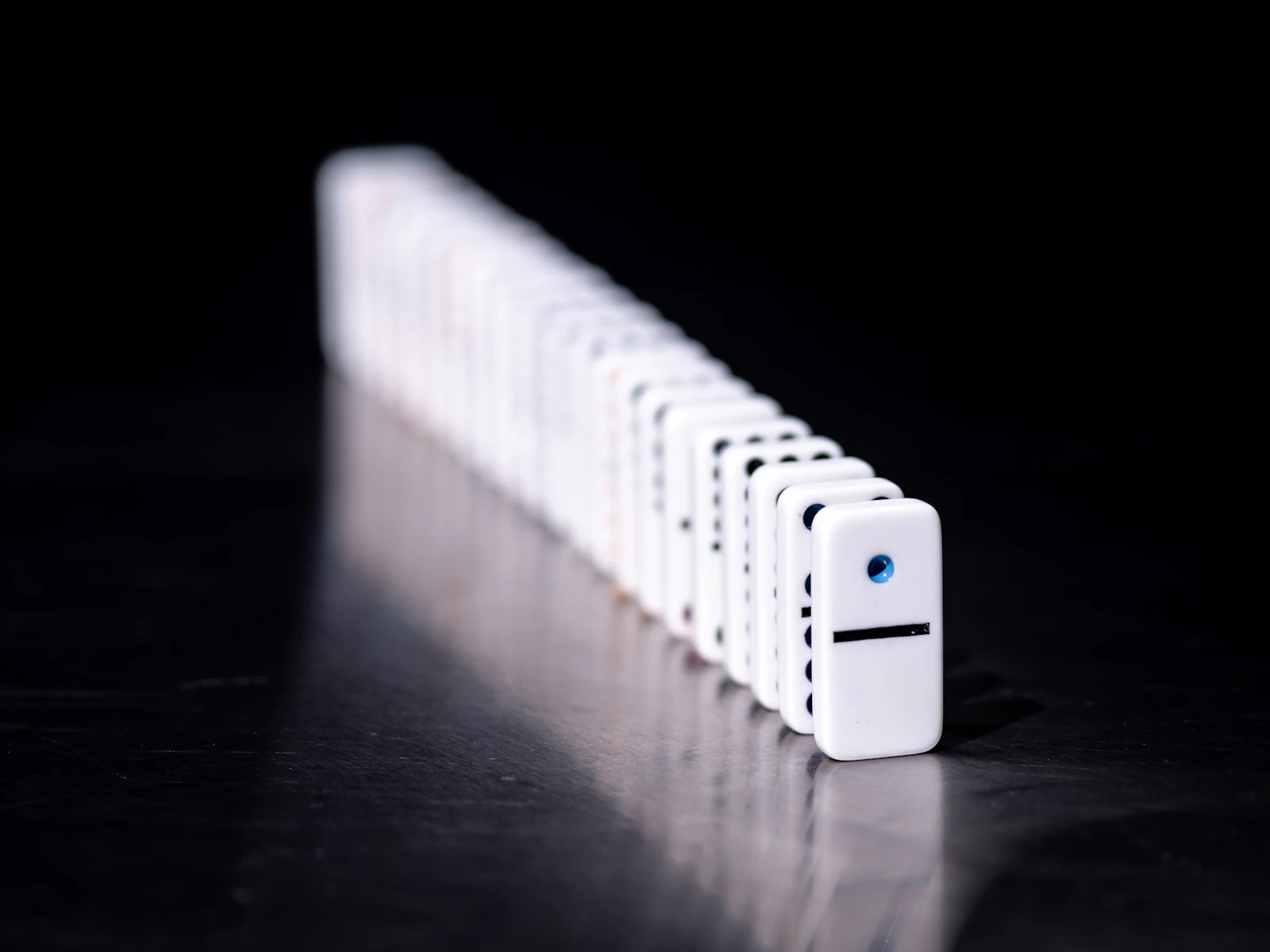 A straight line of white dominoes receding into a dark background