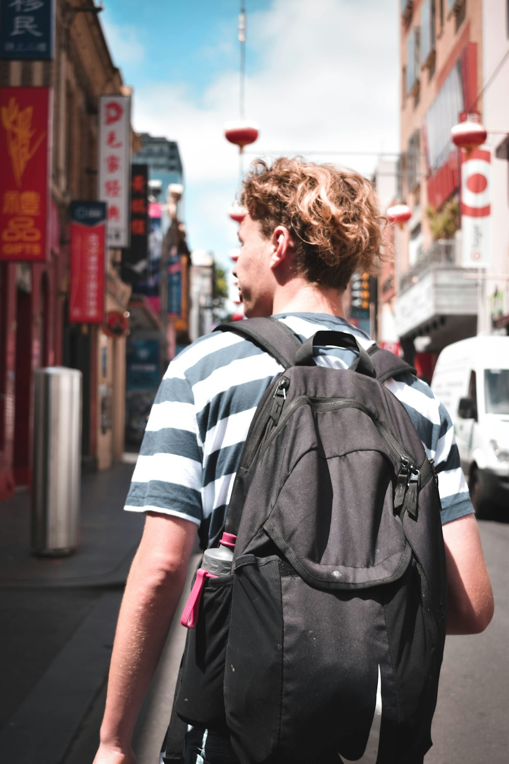 man in black and white striped shirt with black backpack walking on street during daytime