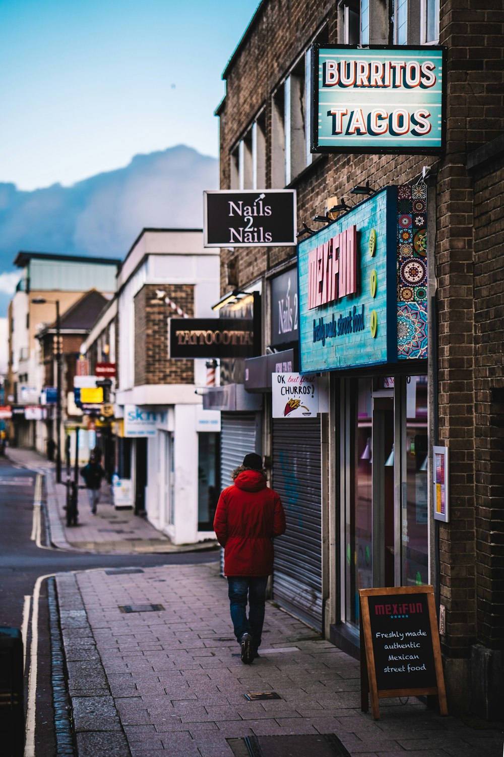 femme en manteau rouge marchant sur le trottoir pendant la journée