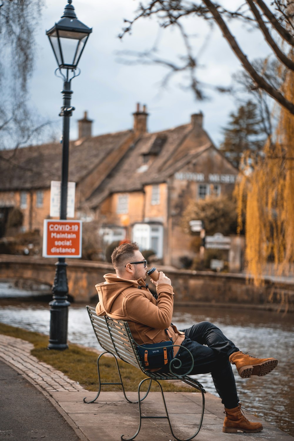 woman in brown jacket and blue denim jeans sitting on brown wooden bench during daytime