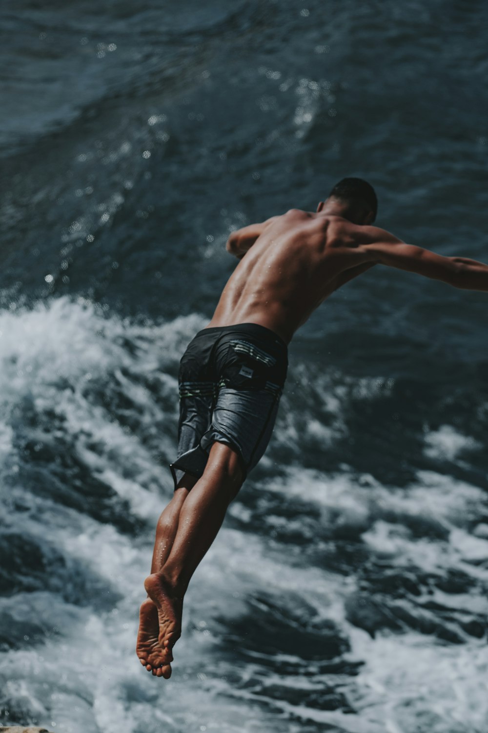 homem de shorts pretos pulando na água