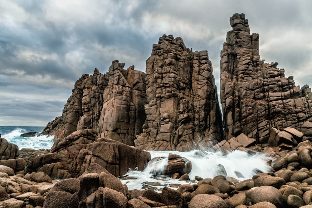 brown rocky mountain near body of water under cloudy sky during daytime