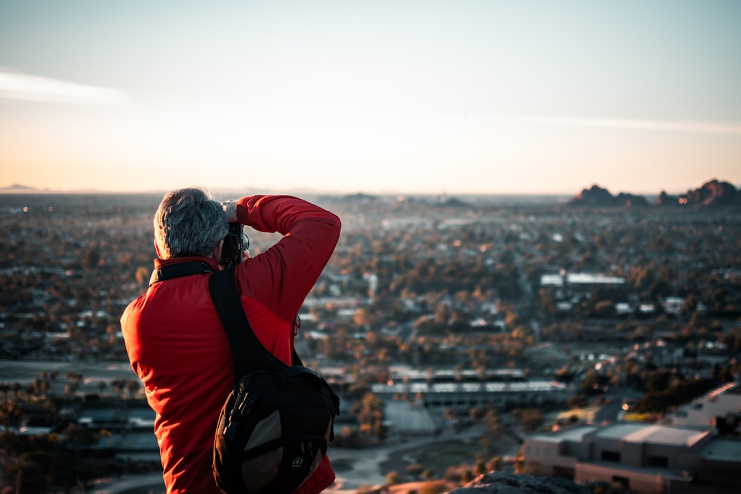 man in red and black jacket sitting on rock looking at city buildings during daytime