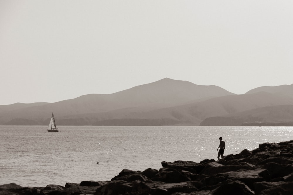 silhouette of 2 people standing on rock near sea during daytime