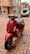 A red scooter is parked in a brick-paved courtyard in front of residential buildings. In the background, there's a silver car with a visible license plate. The area is surrounded by brick walls and large windows.