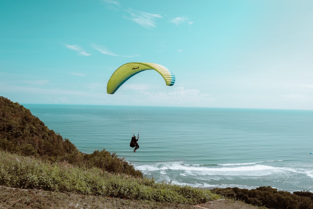 person in black shirt on yellow parachute over blue sea under blue sky during daytime