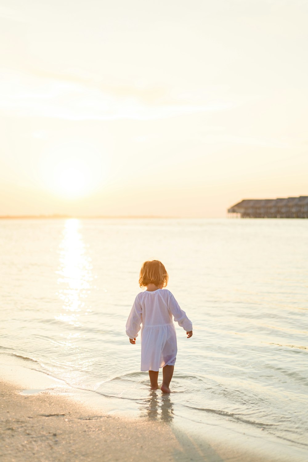 menina na camisa branca de manga comprida e calças brancas em pé na praia durante o dia