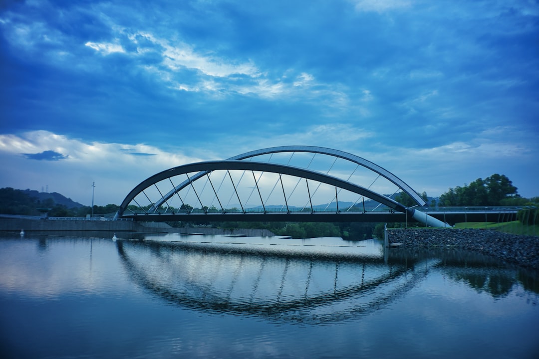 gray metal bridge over river under blue sky during daytime