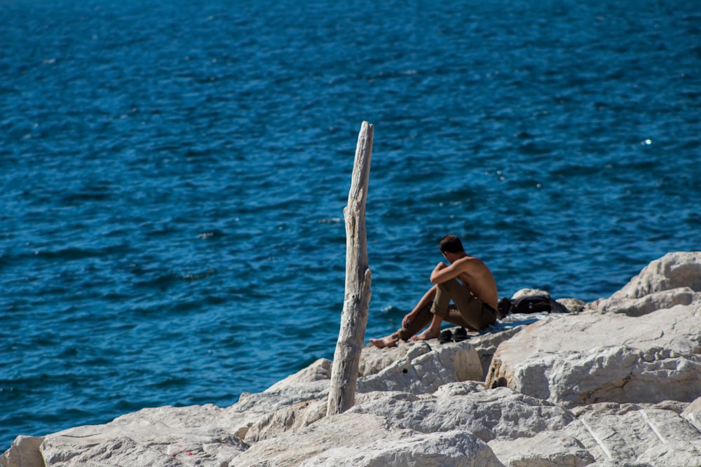 man sitting on rock near body of water during daytime