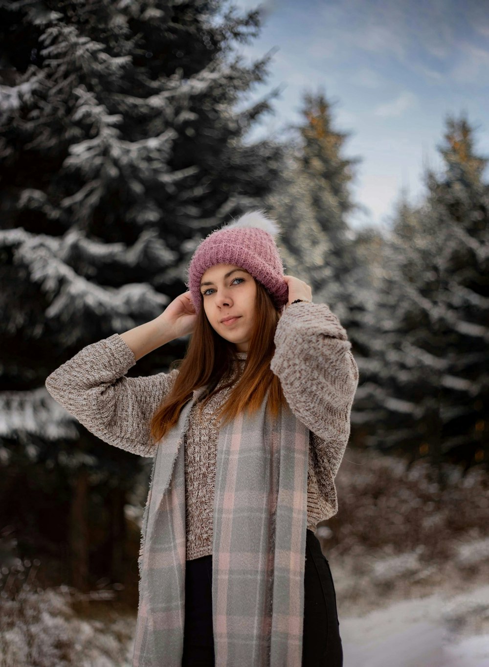 woman in brown and white plaid coat and purple knit cap standing near trees during daytime