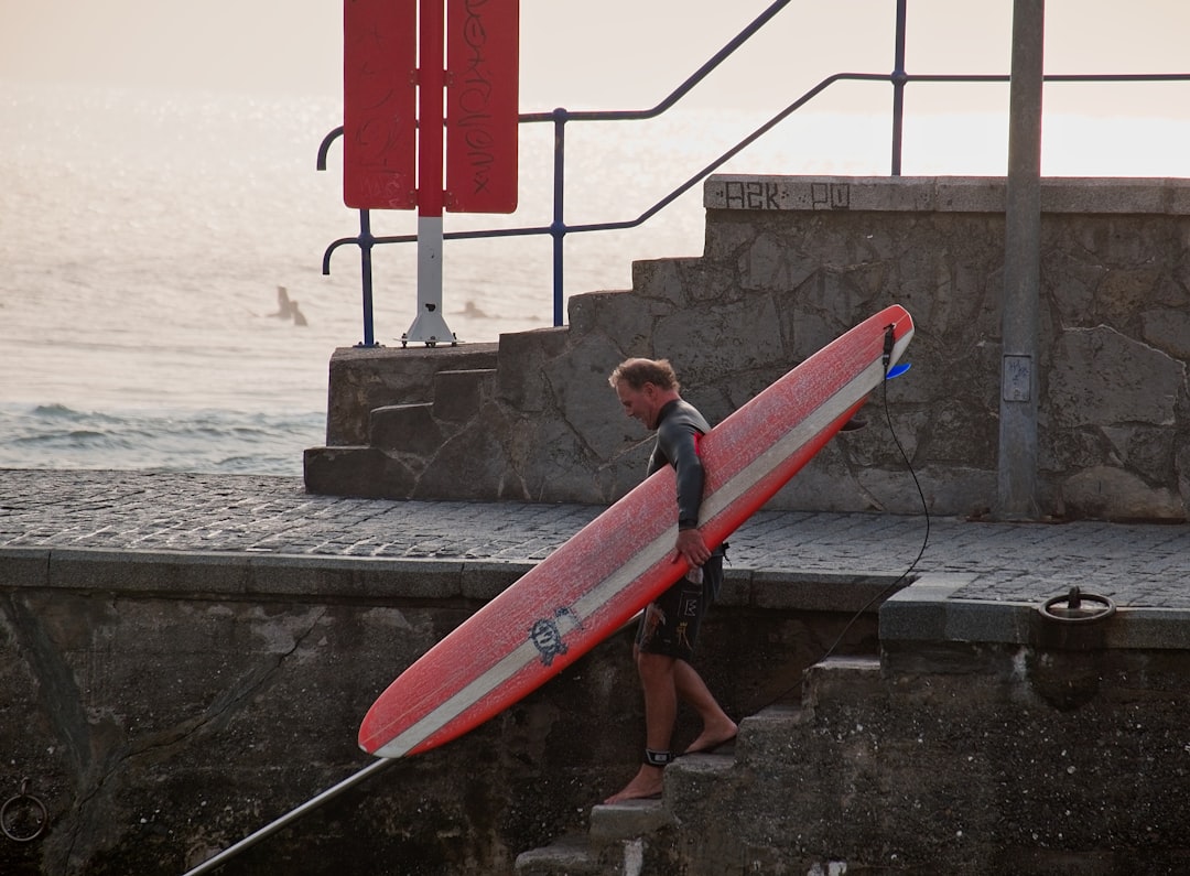 boy in brown hoodie holding red surfboard