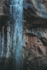 An adventurer rappelling down a waterfall in a lush green canyon.