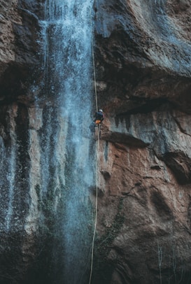 person in blue jacket climbing on rocky mountain during daytime