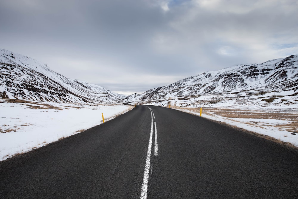 estrada de asfalto preto perto da montanha coberta de neve sob o céu azul durante o dia