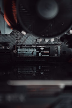 A close-up view of a computer's internal hardware focusing on a Western Digital NVMe solid-state drive installed on a motherboard. The components are sleek, showcasing fine electronic circuits and a smooth black finish.
