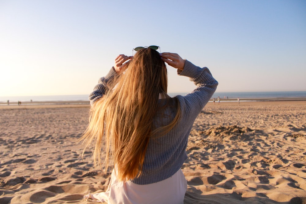 woman in gray sweater standing on beach during daytime