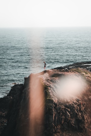 A solo traveler standing on a cliff overlooking a serene sunset beach.