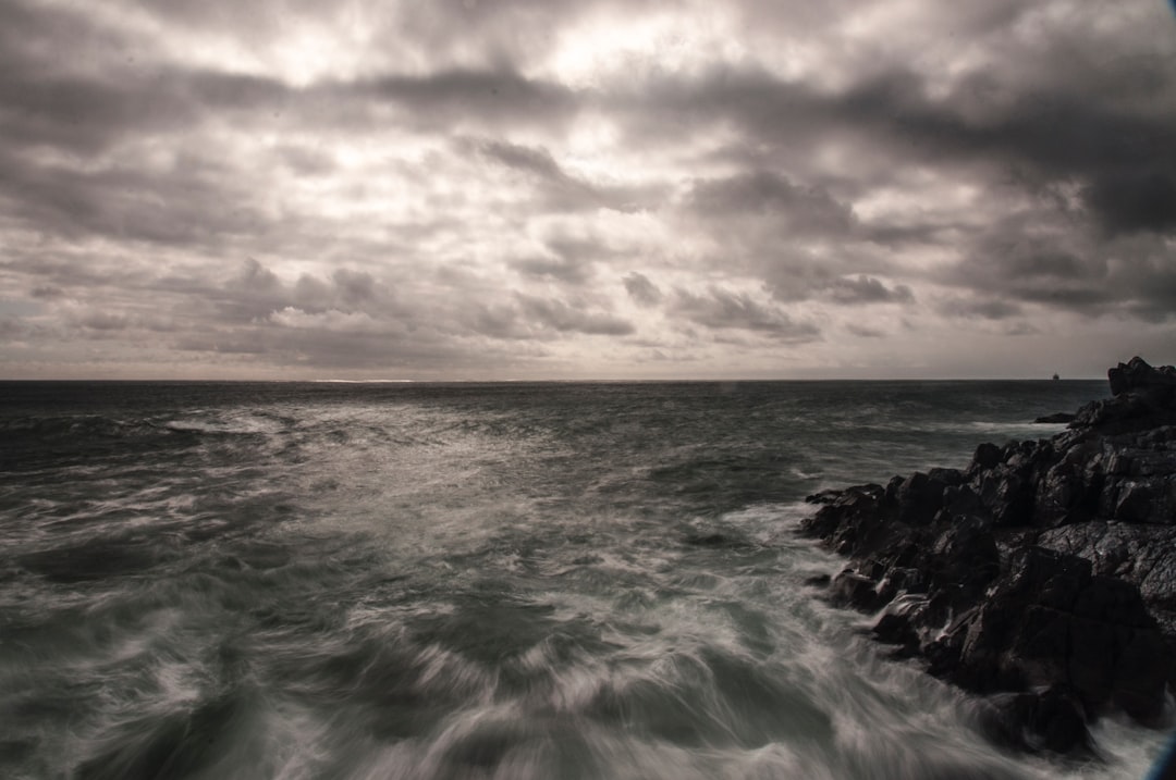 ocean waves crashing on rocks under cloudy sky during daytime