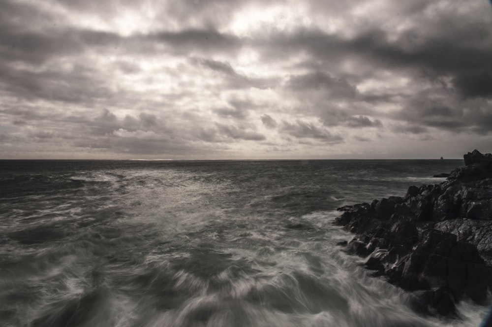 ocean waves crashing on rocks under cloudy sky during daytime