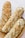 Three rustic loaves of bread with a golden, crusty exterior rest in a woven basket. The bread surface is uneven with a textured crust, suggesting a hearty, artisanal quality.