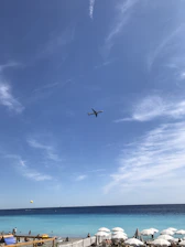 A sleek airplane flying over a turquoise Caribbean sea under a clear blue sky.