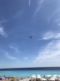 A sleek airplane flying over a turquoise Caribbean sea under a clear blue sky.