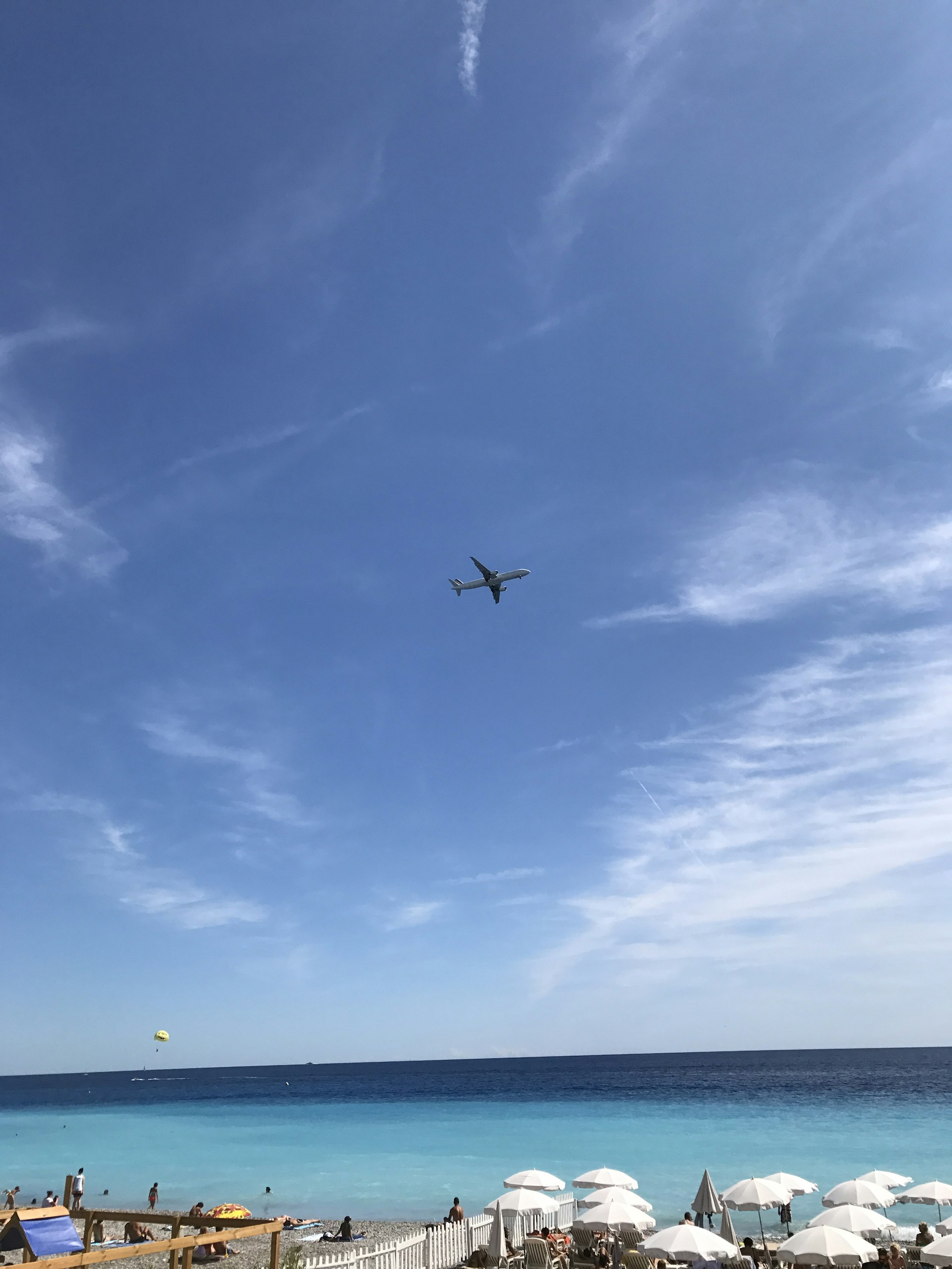 A scenic beach with clear blue water and a small plane flying overhead.