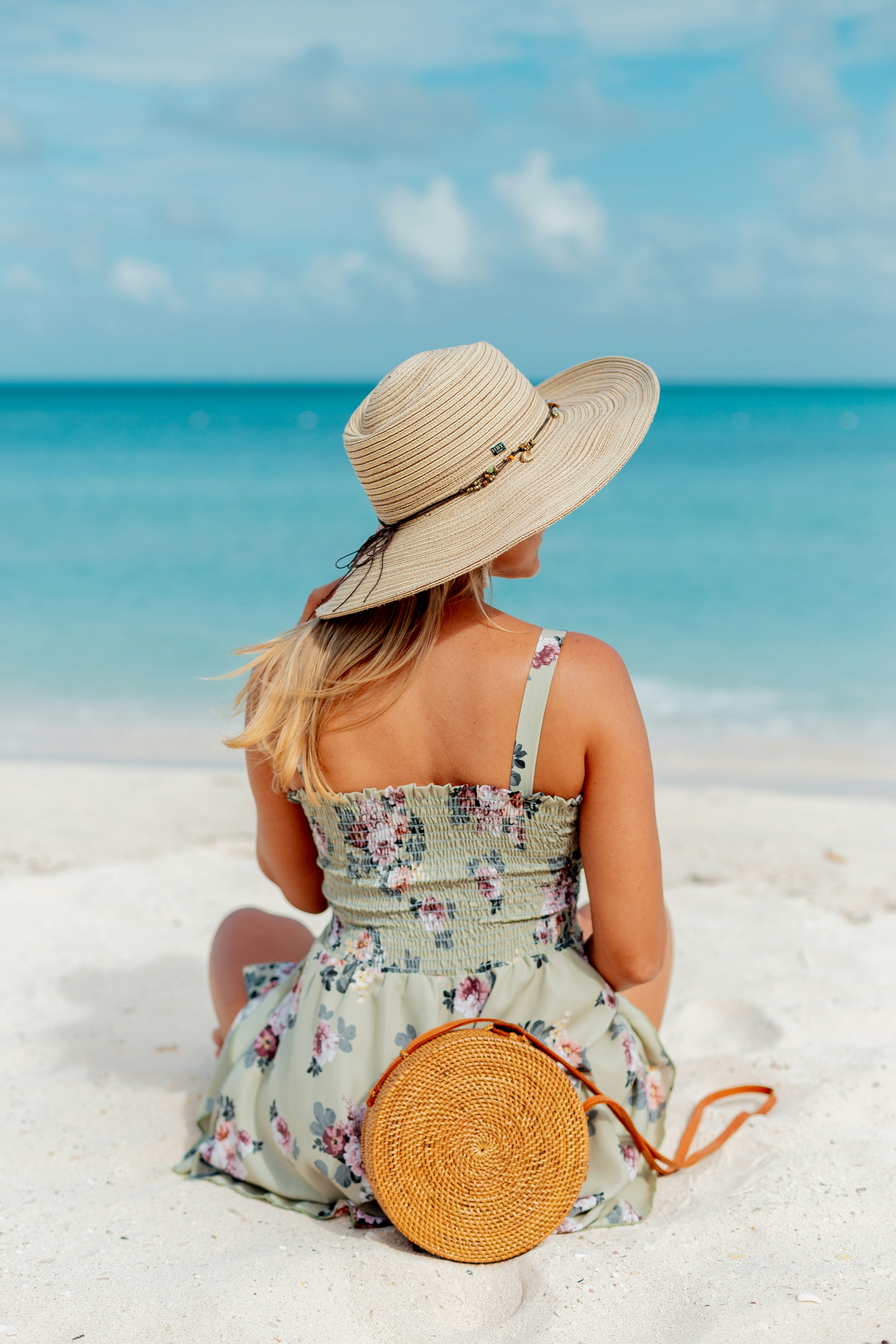 woman in white and pink floral spaghetti strap dress wearing brown sun hat sitting on white