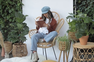 woman in white long sleeve shirt and blue denim jeans sitting on brown wicker armchair reading