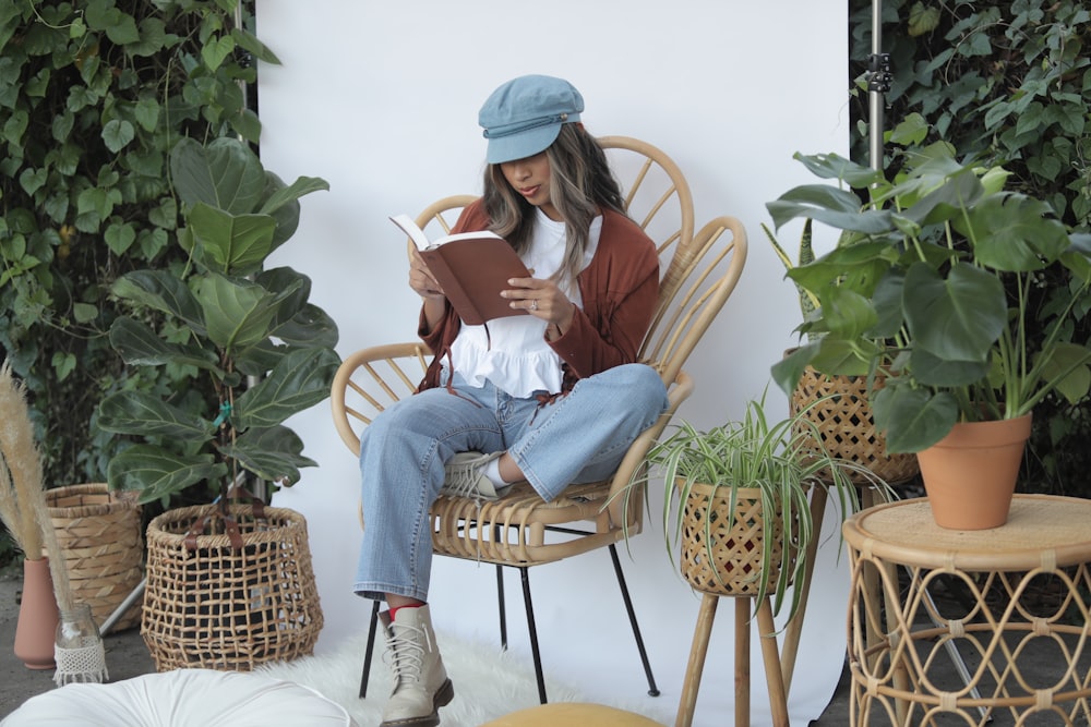 Femme en chemise blanche à manches longues et jean en denim bleu assise sur un fauteuil en osier marron en train de lire