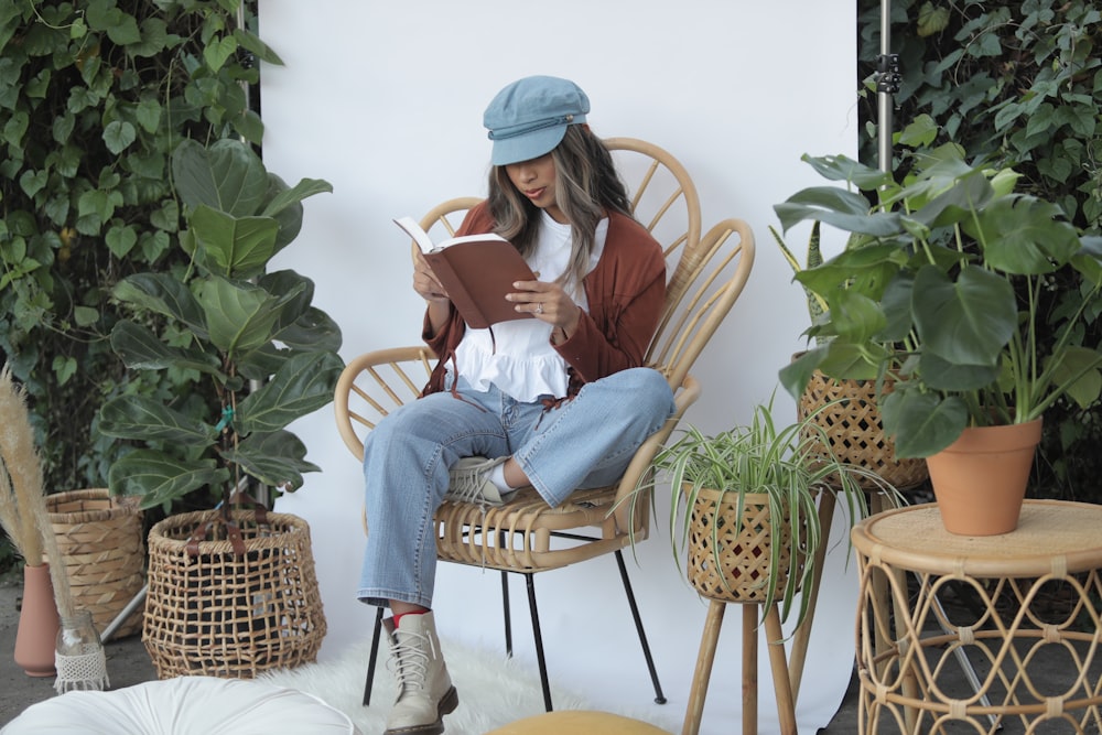 woman in white long sleeve shirt and blue denim jeans sitting on brown wicker armchair reading