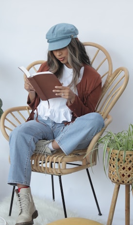 woman in white long sleeve shirt and blue denim jeans sitting on brown wicker armchair reading