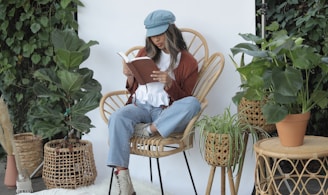 woman in white long sleeve shirt and blue denim jeans sitting on brown wicker armchair reading