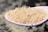 A white spoon holds a heap of uncooked rice grains, with a soft-focus background giving a sense of depth and texture.