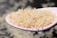 A white spoon holds a heap of uncooked rice grains, with a soft-focus background giving a sense of depth and texture.