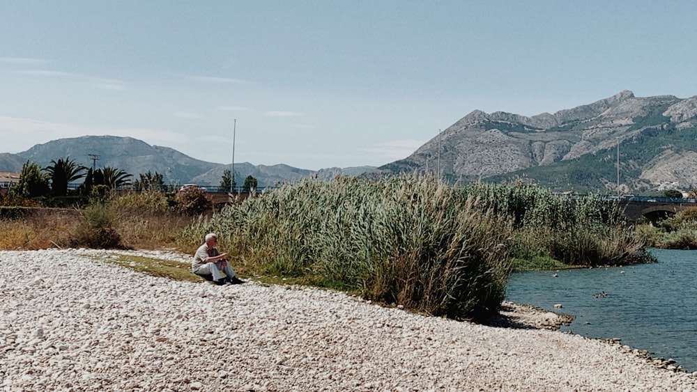 person in red jacket sitting on gray sand near green grass field during daytime