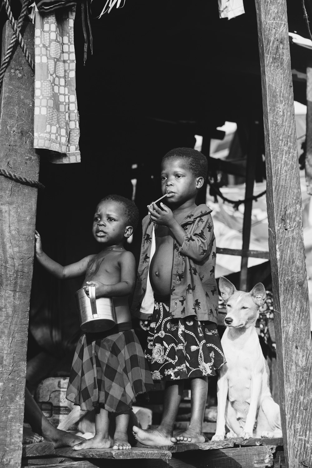 grayscale photo of 2 boys standing beside wooden fence