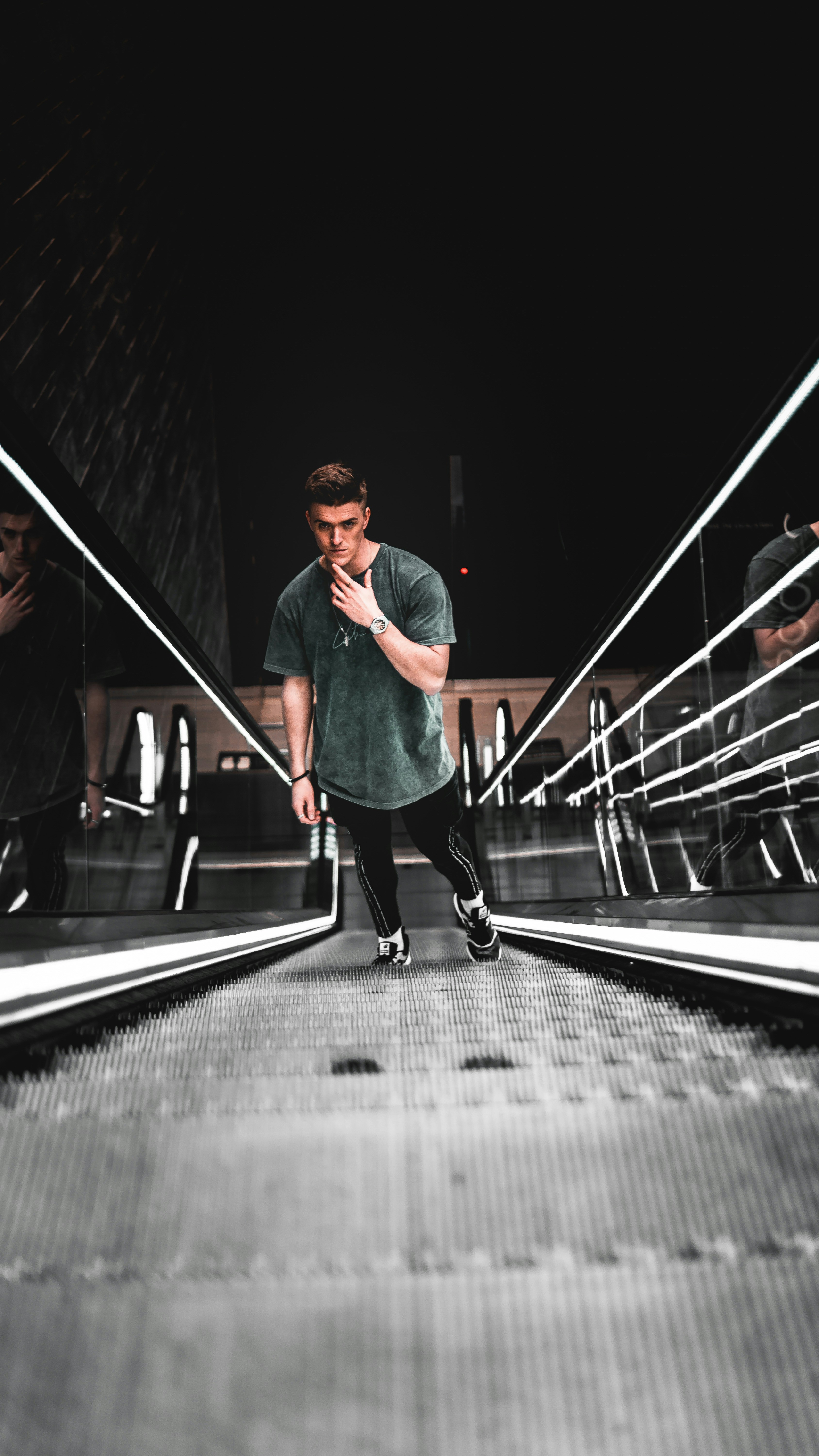 man in green crew neck t-shirt and black pants standing on escalator