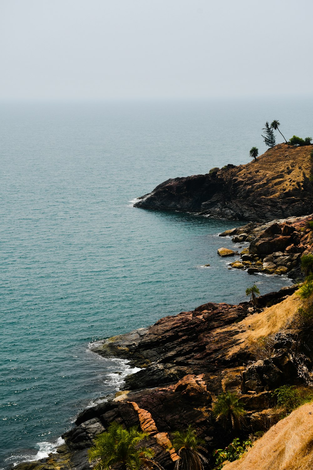 brown rocky mountain beside blue sea during daytime