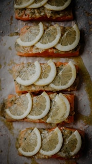 Several pieces of salmon fillets topped with slices of lemon and a seasoning mix, arranged neatly on parchment paper, ready for cooking or baking.