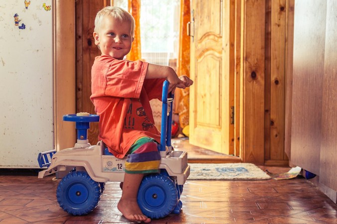 Smiling toddler sitting on a ride-on toy car in a bright hallway