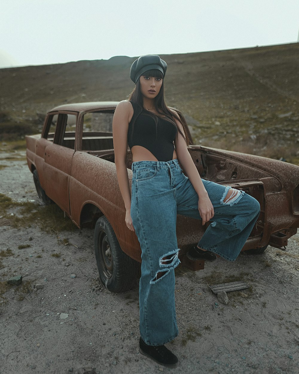 woman in black tank top and blue denim jeans sitting on brown car hood during daytime